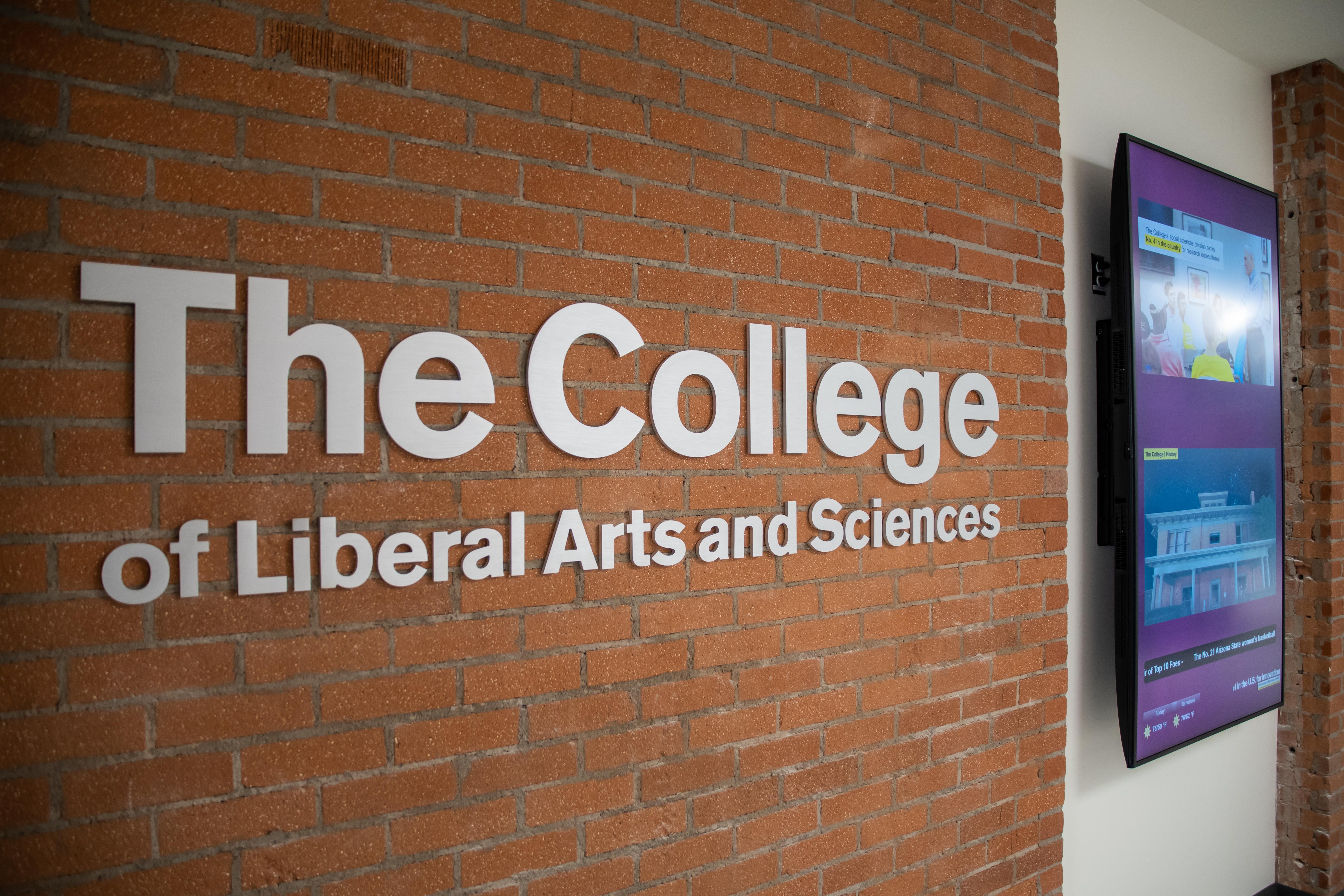Brick wall with white text "The College of Liberal Arts and Sciences" next to a television